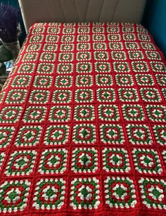 a red and white crocheted blanket sitting on top of a bed next to a plant