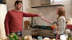 a man and woman in the kitchen pointing at each other's hand with wine glasses on the counter