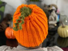 a person wearing an orange knitted hat with a green leaf on it's back