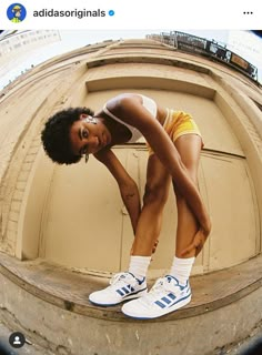 a woman in yellow shorts and white sneakers posing for a selfie with her tennis shoes