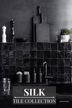 a kitchen sink with black tiles and cutting board on the wall above it, surrounded by other items