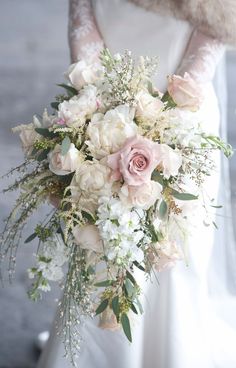 a bridal bouquet with white flowers and greenery is held by a fur stoler