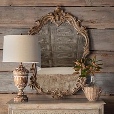 an antique dresser with a lamp and mirror on it, next to a plant in a vase