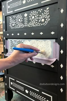 a person using a blue pen to paint a black cabinet with white stencils