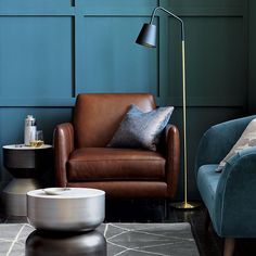 a living room with two chairs and a lamp in front of a blue paneled wall