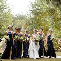 a group of women standing next to each other in front of trees and bushes with bouquets