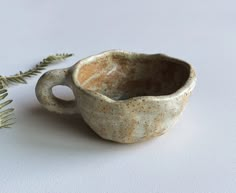 a ceramic cup sitting on top of a white table next to a green leafy plant