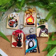 four keychains with different designs on them sitting next to some plants and leaves