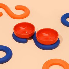 two orange and blue bowls sitting next to each other on top of a white surface