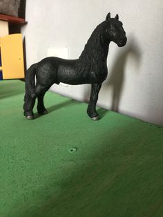 a small black horse standing on top of a green floor next to a white wall