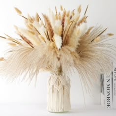 a vase filled with dry grass next to two books