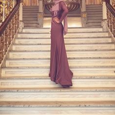 a woman in a long dress standing on the stairs with her hand on her hip