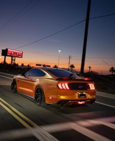 an orange mustang driving down the road at night with its lights on and taillights on