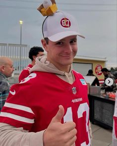 a man in a football jersey giving the thumbs up sign while wearing a white hat