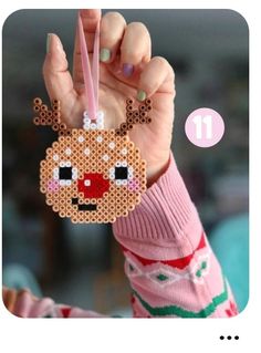 a person holding up a beaded ornament with a reindeer face on it