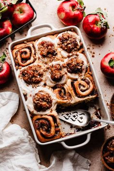 an apple cinnamon roll in a baking dish with apples around it and on the side