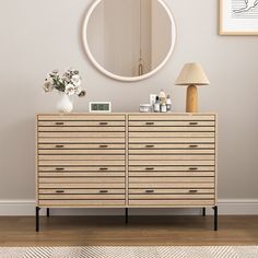 a dresser with drawers and a mirror on the wall above it, in front of a lamp