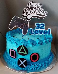 a blue birthday cake decorated with video game controllers and happy birthday sign on top, sitting in a cardboard box