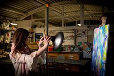 a woman holding a black object in front of her face while standing next to an easel