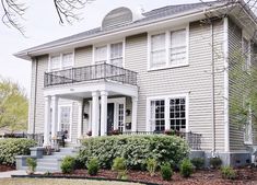 a large house with white trim and black balconies on the second story, surrounded by shrubbery