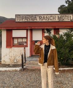 a woman standing in front of a red and white building with a sign that reads topanga ranch motel