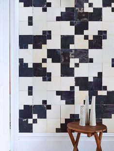 two vases sitting on a small table in front of a wall with black and white tiles