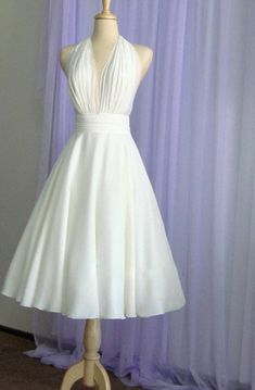 a white dress on a mannequin stand in front of purple curtained background