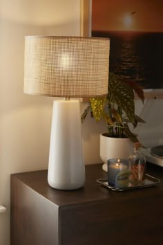 a white lamp sitting on top of a wooden table next to a potted plant