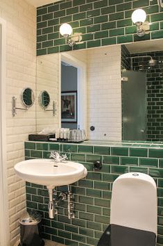 a green tiled bathroom with a white sink and black countertop, along with two mirrors on the wall