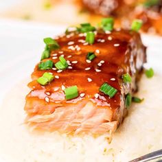 a piece of salmon covered in sauce and green onions on top of rice with a fork