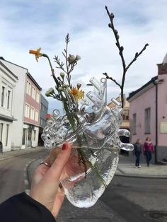 a person holding up a vase with flowers in it on the side of a road