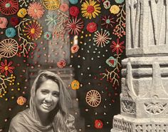 a woman standing in front of a wall with flowers on it and an ornamental structure behind her