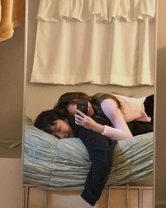 two women are laying on a bed looking at their cell phones in front of the mirror