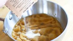 a person is sprinkling sugar on food in a saucepan with a wooden table