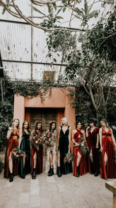 a group of women standing next to each other in front of a building with greenery