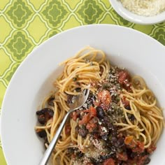 a white bowl filled with pasta and sauce on top of a green tablecloth next to a spoon