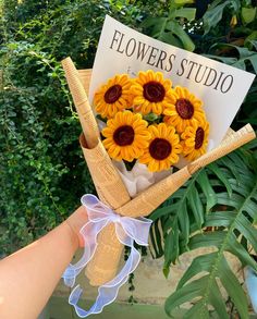 a bouquet of sunflowers is held up by someone's hand with a sign in the background