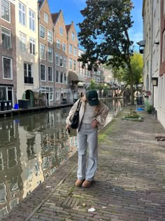 a woman walking down a brick sidewalk next to a body of water with buildings in the background