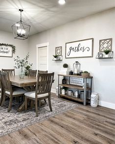 a dining room table and chairs in front of a white wall with framed pictures on it