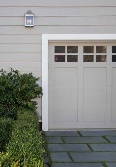 a white garage door with two windows and a light on the side of it in front of a house