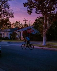 a person riding a bike down the street at dusk with a stop sign in front of them