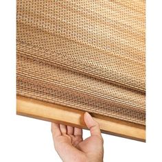 a hand is holding up the edge of a bamboo window covering that's partially closed