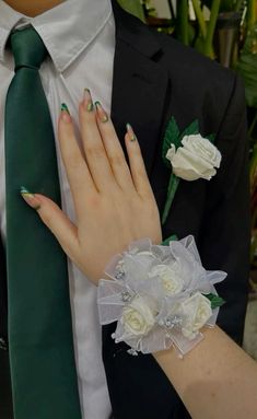 a woman wearing a green tie with white flowers on her wrist and two roses attached to the man's lapel