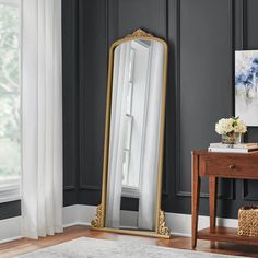 a large gold framed mirror sitting on top of a wooden table next to a window