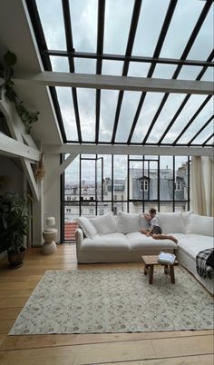 a man sitting on top of a white couch in a living room next to a window