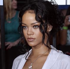 a close up of a person wearing a white shirt and necklace with people in the background