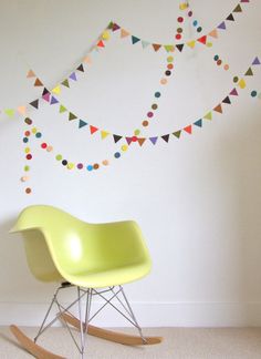 a yellow rocking chair in front of a white wall with multicolored bunting