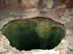 a hole in the ground that is filled with green water and dirt, surrounded by rocks