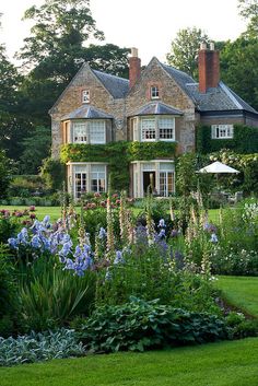 a large house surrounded by lots of flowers and greenery in front of the house