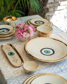 a table topped with plates and bowls covered in gold rimmed dishes next to a potted plant